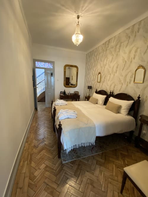 Camas de solteiro com roupa branca em quarto elegante de hospedaria em Coruche, assoalho em espinha, espelhos ornamentados e lustre de cristal