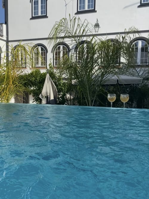 Crystal-clear swimming pool at Patio Da Villa guesthouse in Coruche, with white building, lush tropical plants, and poolside