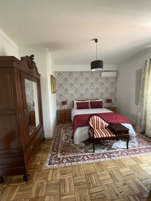 Elegant bedroom at Patio Da Villa guest house in Coruche with burgundy bedding, damask wallpaper, dark wood wardrobe, and