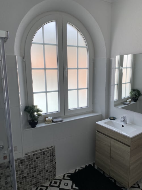 Modern bathroom with arched window, white sink vanity, and small potted plants at Patio Da Villa guest house in Coruche