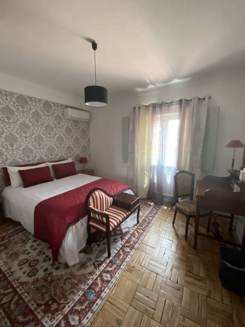 Quarto elegante na pousada Patio Da Villa em Coruche com acentos vermelhos, papel de parede com padrão damasco e portas francesas com vista para