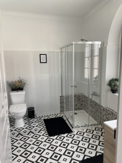 Modern bathroom with geometric black and white floor tiles, white subway tile walls, glass shower enclosure, and potted