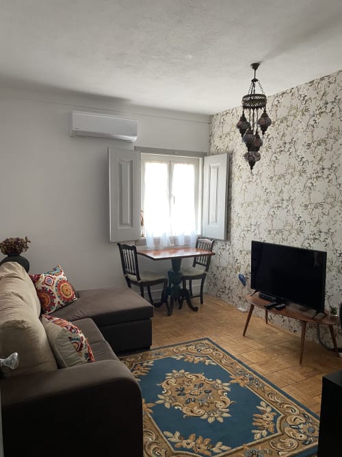 Cozy living room at Patio Da Villa guest house with gray sofa, floral wallpaper, TV, dining table, and decorative pendant