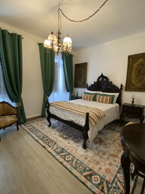 Quarto Deluxe Duplo elegante no Patio Da Villa com cama preta ornamentada, cortinas verdes e lustre de latão