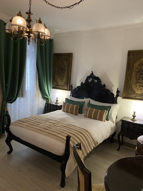 Luxurious bedroom at Patio Da Villa with black ornate bed, green curtains, brass chandelier, and elegant furnishings in