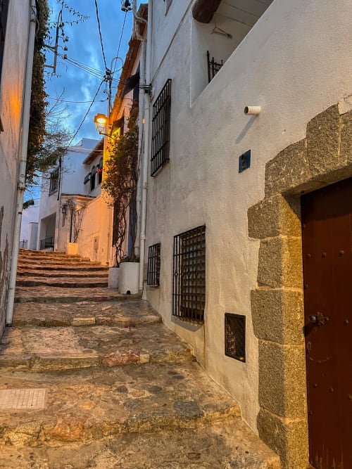 Estret carrer empedrat a Palafrugell amb cases blanquejades, portes de fusta i llum vespertina a Finques Garcia