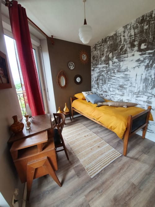 Chambre élégante aux Forges Du Lou avec literie jaune, meubles en bois, papier peint bouleau et rideaux rouges