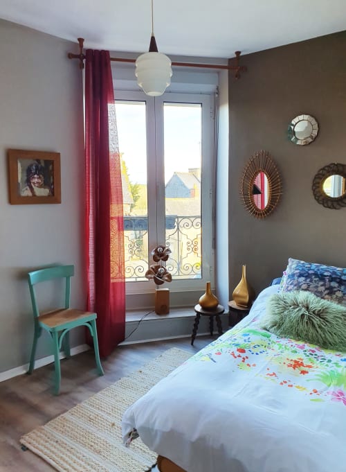 Chambre éclectique aux Forges Du Lou avec fauteuil turquoise, literie colorée, miroirs ornés et vue sur balcon parisien