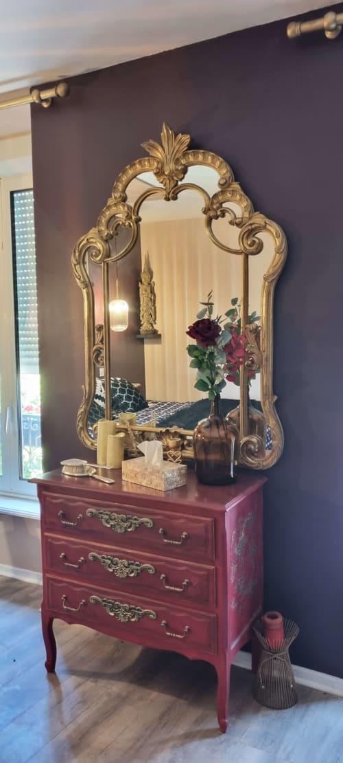 Miroir doré aux ornements élaborés au-dessus d'une commode bordeaux dans la suite L'Antre de Belenos aux Forges Du Lou, Jugon-les-Lacs