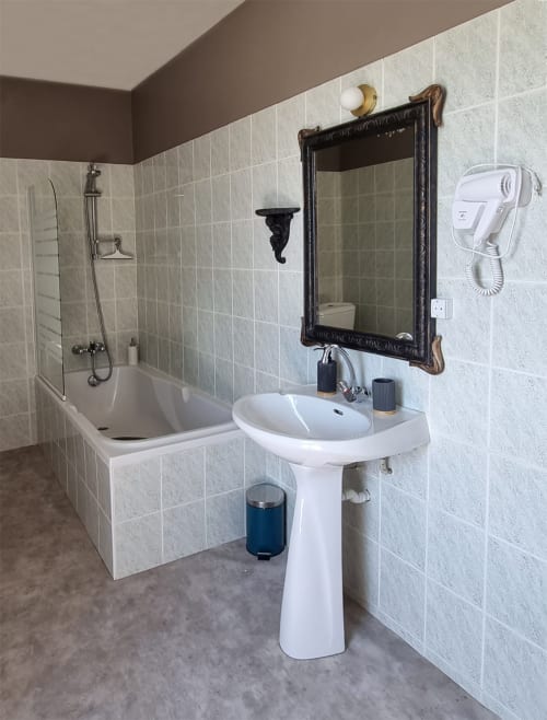 Salle de bain moderne aux Forges Du Lou avec lavabo sur piédestal, baignoire, douche, miroir encadré et sèche-cheveux à Jugon-les-Lacs