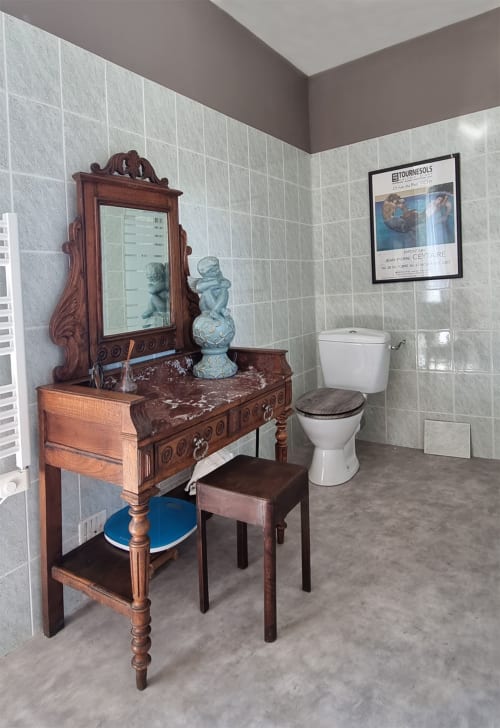 Salle de bain vintage de la suite Les Forges Du Lou avec vanité en bois ouvragé, miroir, figurines céramiques décoratives et équipements modernes