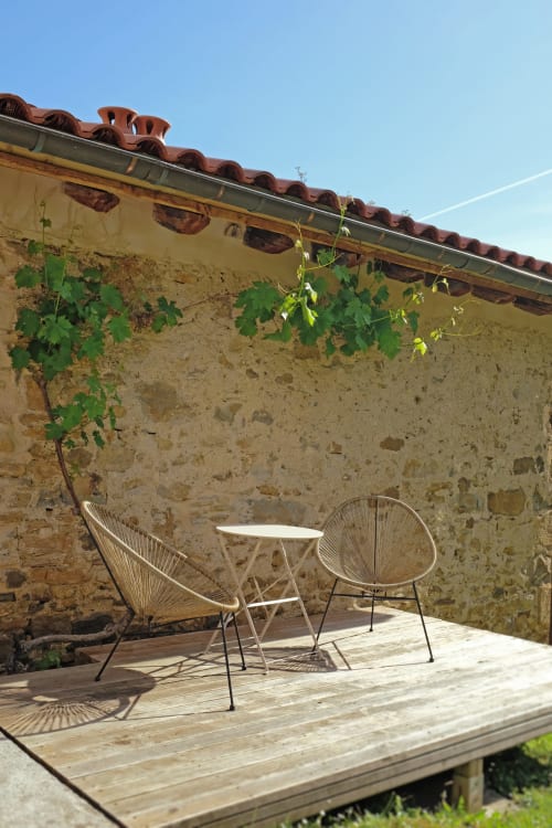 Terraza rústica de piedra en Casa rural Mañarinegi con sillas tejidas, mesa de madera y enredaderas bajo cielo azul