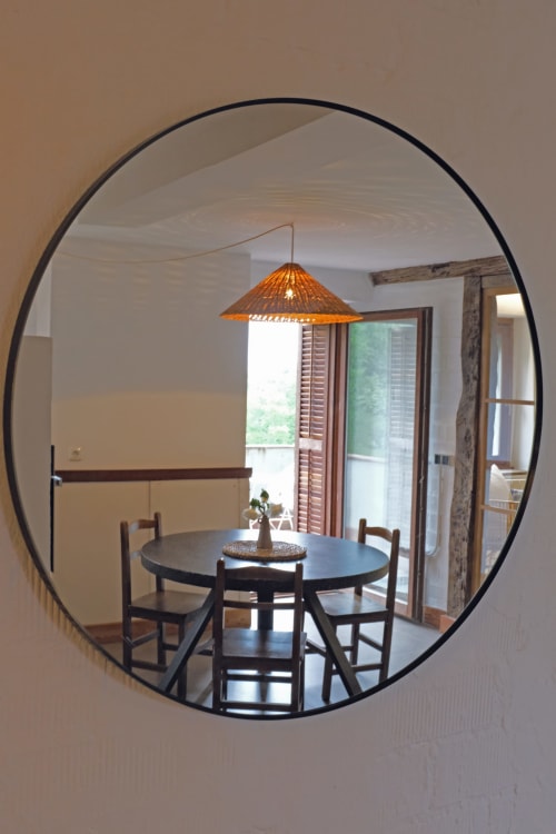 Comedor con mesa redonda negra y lámpara colgante tejida naranja, reflejada en espejo circular moderno de Casa rural