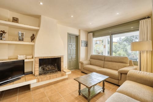 Spacious living room with fireplace, beige sofas, and garden views at Finques Garcia Enrich cottage near Palafrugell beach
