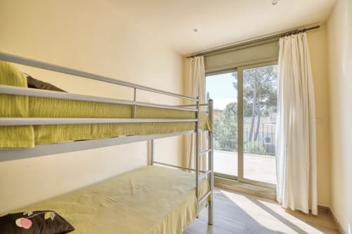 Bright bedroom with bunk beds, yellow linens, and glass doors opening to a terrace with sea views in Palafrugell cottage.