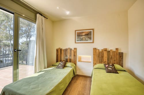 Twin bedroom with yellow bedding and wooden headboards, garden view doors, and fireplace at beachside cottage in Palafrugell