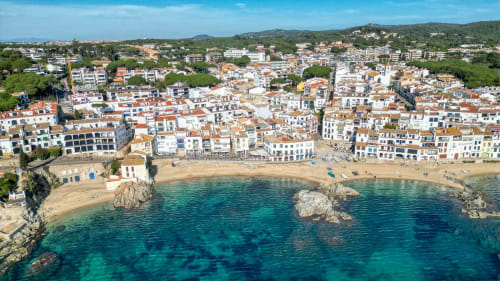 Aerial view of Palafrugell beachfront with sandy cove, turquoise Mediterranean waters, and white apartment buildings on the