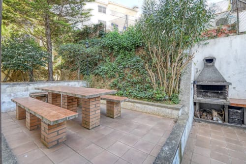 Outdoor patio at Finques Garcia Enrich in Palafrugell with brick picnic tables, barbecue grill, and lush garden surrounded by