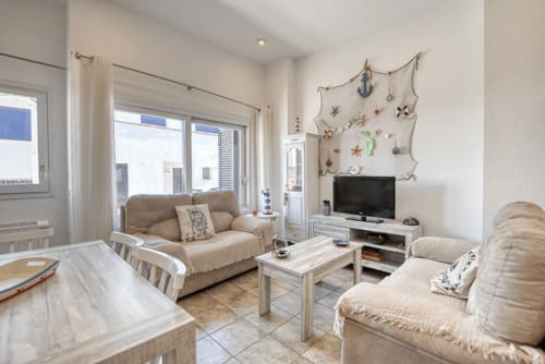 Bright living room in Palafrugell apartment with beige furnishings, TV, wooden furniture, and nautical wall decor