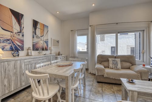 Bright apartment living area in Palafrugell with dining table, beige sofa, sailboat artwork, and ocean views from terrace