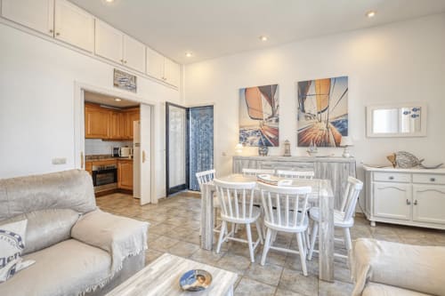 Bright open-plan apartment living area in Palafrugell with dining table, white chairs, wooden furniture, nautical sailboat