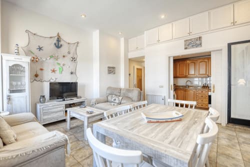 Bright open-plan living area in Palafrugell apartment with dining table, seating, TV, kitchenette and nautical decor