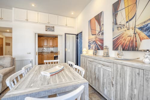 Bright dining room with wooden table, nautical wall art, and kitchen access at Finques Garcia Enrich apartment in Palafrugell