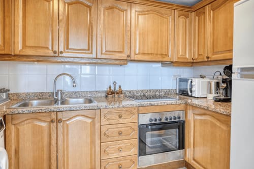 Modern kitchen with wooden cabinets, granite countertops, stainless steel oven and sink at Finques Garcia Enrich apartment,
