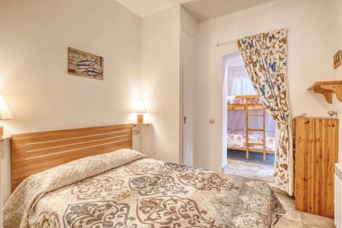 Cozy bedroom in Palafrugell apartment with wooden bed, warm lighting, and doorway to adjacent room with bunk bed