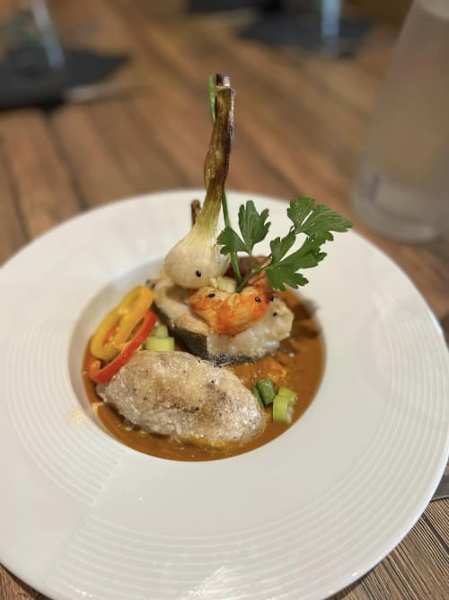 Plat élégamment dressé à l'hôtel La Romance avec viande saisie, crevettes, légumes et sauce à Bagard