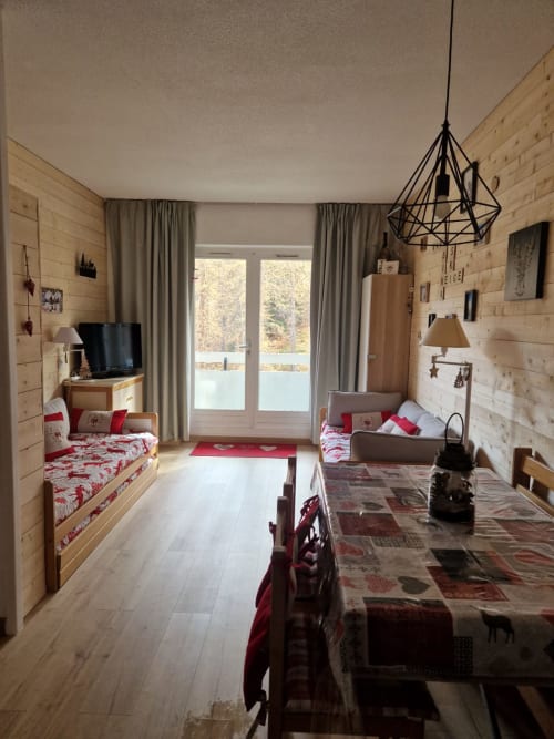  "Salon de l'appartement 214 à Vars-les-Claux, avec un mur refait en bois apportant une touche chaleureuse et authentique, créant une atmosphère cosy et montagnarde pour se détendre après une journée de ski."
