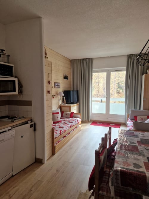"Salon de l'appartement 214 à Vars-les-Claux, avec un mur en bois naturel qui crée une ambiance chaleureuse et montagnarde, offrant un cadre idéal pour se relaxer après une journée sur les pistes."
