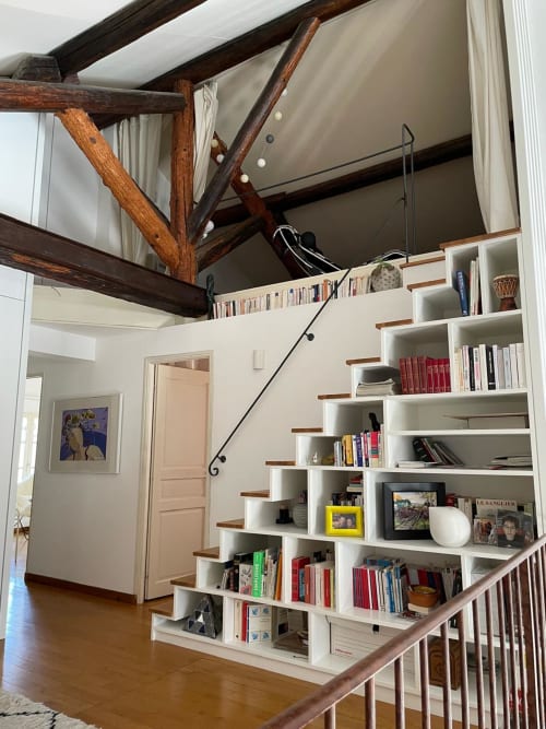 Modernes Villeninterieur mit sichtbaren Holzbalken, weißen Einbauregaln und Holztreppe in La Conciergerie De