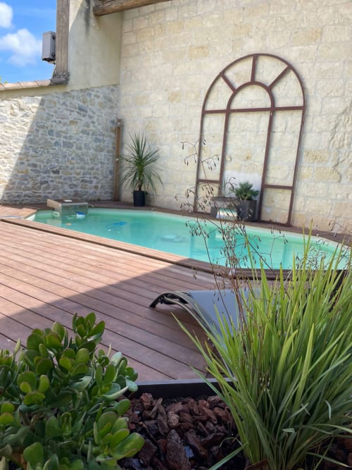 Piscine turquoise avec terrasse en bois entourée de plantes et murs de villa en pierre rustique à La Conciergerie De Franck à Boissieres