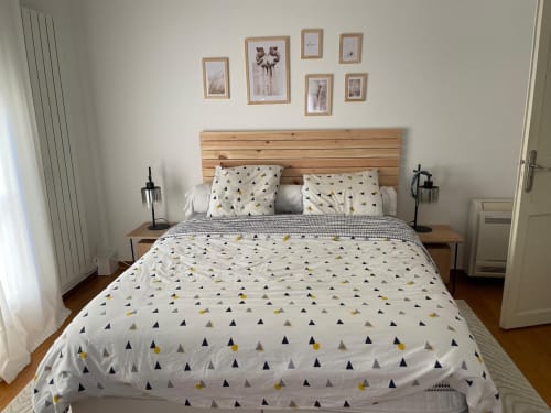 Helles modernes Schlafzimmer der Villa La Conciergerie De Franck mit Holzkopfteil, gemusterter Bettwäsche und botanischen Rahmen