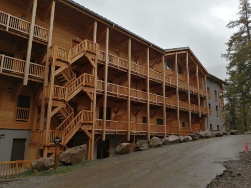 "Vue extérieure du bâtiment de l'appartement 203 à Vars-les-Claux, avec une architecture montagnarde typique, entouré de paysages alpins, idéalement situé pour accéder aux pistes et profiter de la station."
