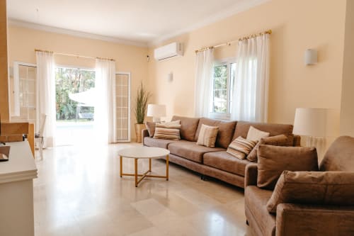 Sala luminosa en la cabaña Las Golondrinas con sofá de cuero marrón, vistas al jardín y comodidades modernas