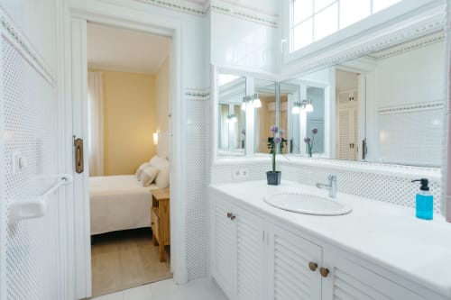 Baño moderno con tocador blanco, espejo grande y acceso al dormitorio en la casa rural Las Golondrinas, Cap d'Artrutx