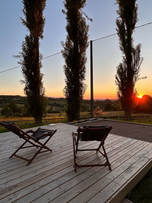 Wooden deck with lounge chairs overlooking sunset and countryside at Domaine de Blanvatel, Saint Pierre en Auge