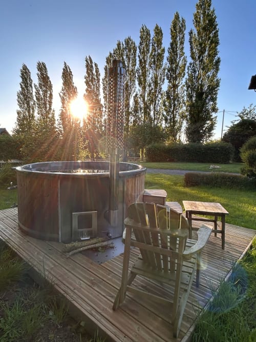 Rustic hot tub on wooden deck at Domaine de Blanvatel with poplar trees and garden seating at sunset