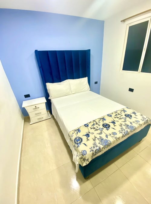 Habitación moderna del hotel Casa Mango en Cali con cabecera de terciopelo azul, ropa de cama blanca y manta floral