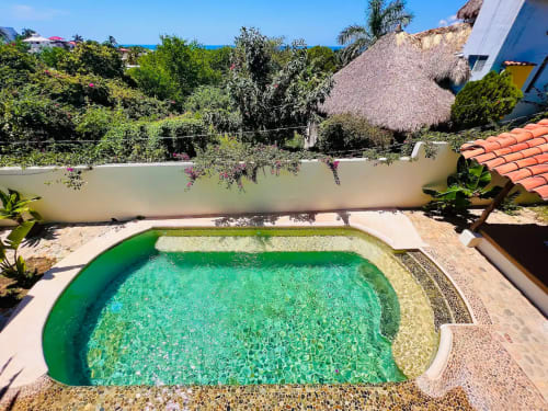 Piscina turquesa del hotel Calilla & Tsuki en Puerto Escondido con paredes blancas, jardín tropical y vista al océano