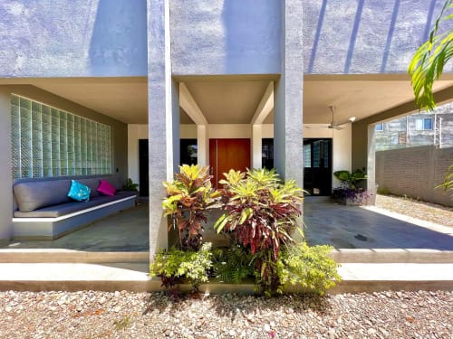 Moderno patio cubierto del hotel Calilla & Tsuki en Puerto Escondido con plantas tropicales, zona de estar y puerta de madera roja