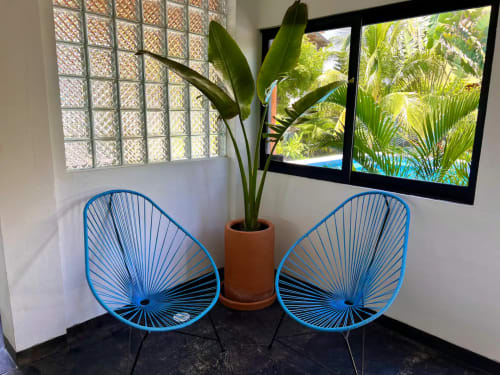 Luminosa zona de descanso en Calilla & Tsuki Puerto Escondido con dos sillas azules, plantas decorativas y vistas tropicales.