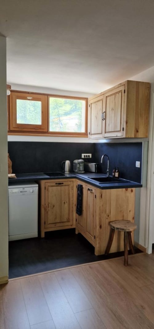  "Cuisine moderne de l'appartement à Vars-les-Claux, alliant des éléments noirs élégants et des touches de bois naturel, créant un espace à la fois chic et chaleureux, entièrement équipé pour préparer des repas conviviaux."