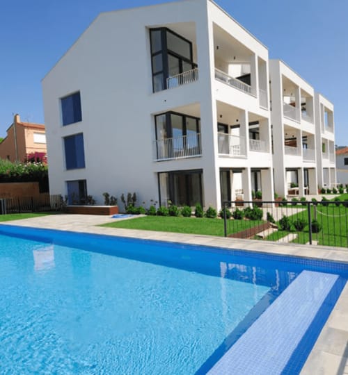 Immeuble blanc contemporain aux fenêtres bleues dominant une piscine à Palafrugell