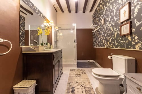 Salle de bain élégante à Casa Peregrinando avec vanité en bois foncé, fleurs jaunes, papier peint à motifs et douche ouverte
