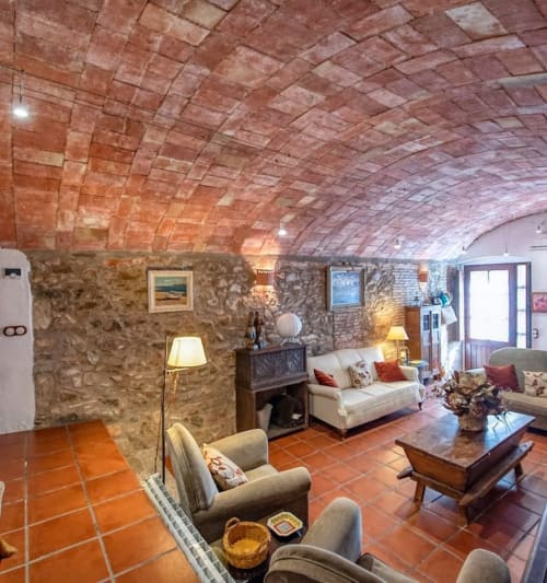 Rustic vaulted stone lounge at Finques Garcia Enrich hotel in Palafrugell with terracotta floors, cream sofas, and warm