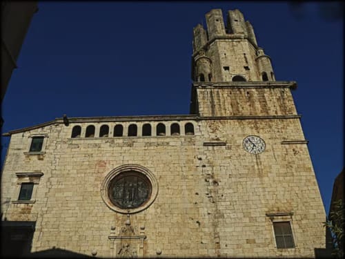 Historic stone church tower in Palafrugell with illuminated facade against blue sky