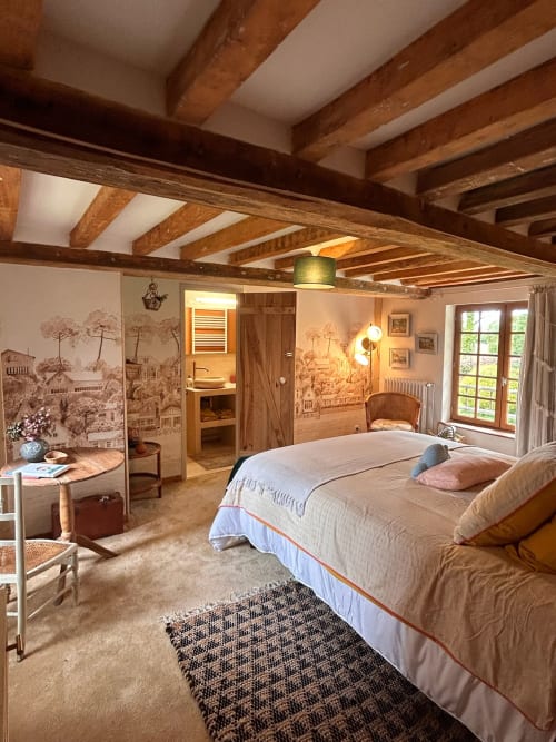 Spacious bedroom at Domaine de Blanvatel B&B with exposed wooden beams, queen bed, and ensuite bathroom in Saint Pierre en